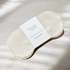 An Arthur Betsy sleep mask made of soft, lustrous champagne-colored fabric, wrapped in a white paper band with the brand name 'ARTHUR BETSY' printed in black. Part of the Sleepover Macaron Gift Set.