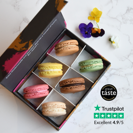 A gift box of six classic macarons in various colors including pistachio, chocolate, lemon, vanilla, raspberry, and salted caramel flavors.