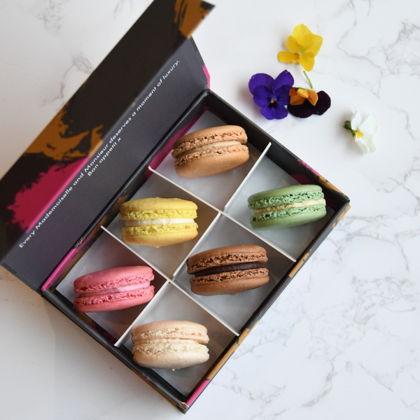 Box of colorful macarons on a marble surface with flowers.