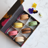 Box of colorful macarons on a marble surface with flowers.