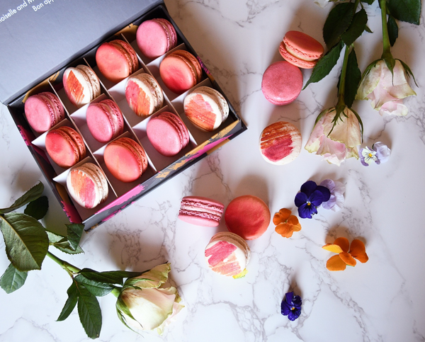 pinks and reds macarons in gift box with flowers surrounding it