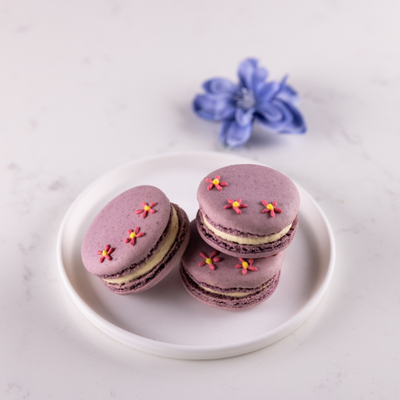 Raspberry & basil macarons with light purple shells and pink royal icing flower decorations, created for Mother’s Day gifting
